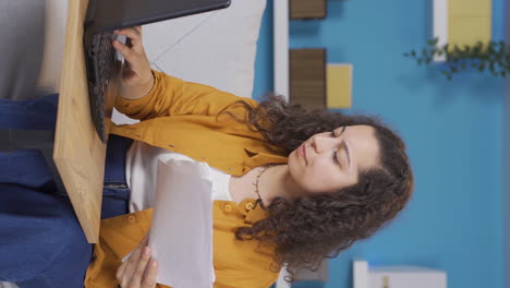 Vertical-video-of-Young-woman-working-on-laptop-throws-files-angrily.